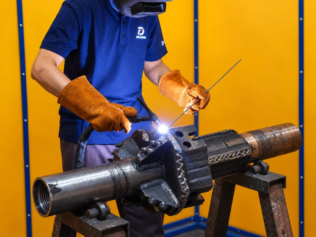 Welder fabricating a Fixed Type Hole Opener in an industrial welding booth