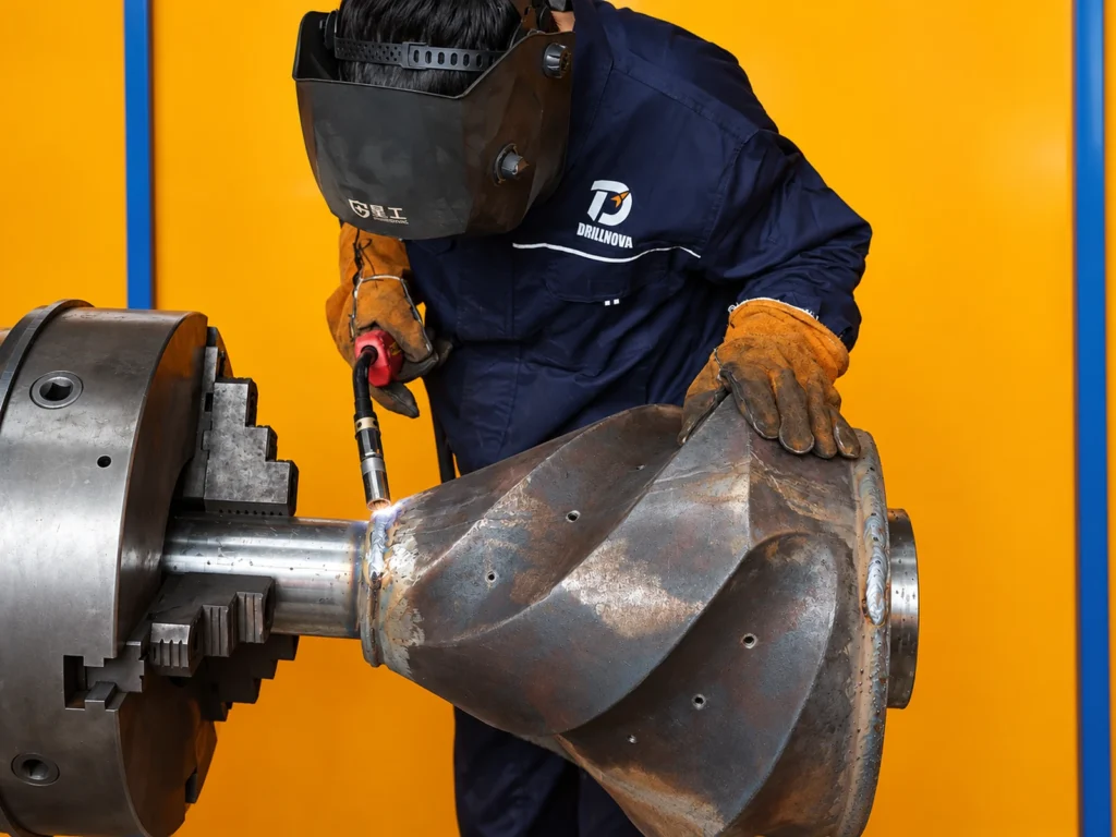 Technician welding a large HDD tool component on a rotary fixture